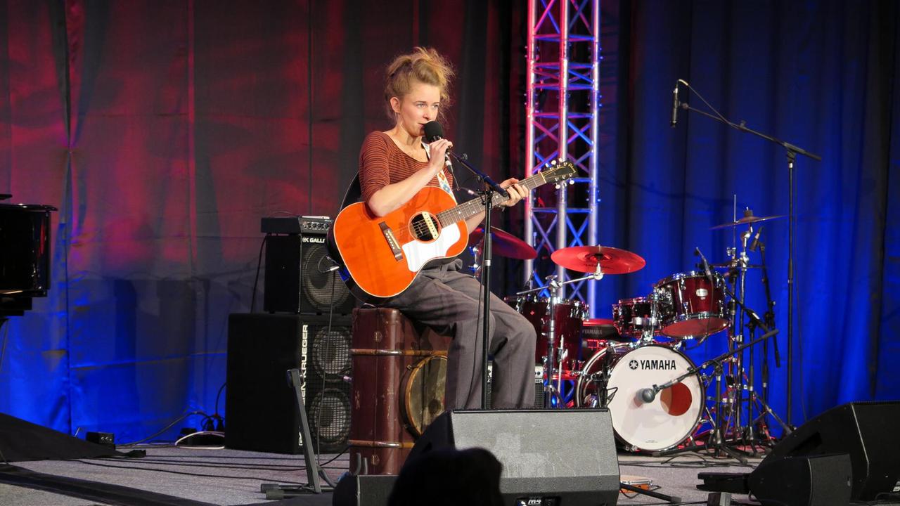 Lucie Mackert sitzt auf der Bühne mit Gitarre und singt Lucie Mackert sitzt auf der Bühne mit Gitarre und singt
