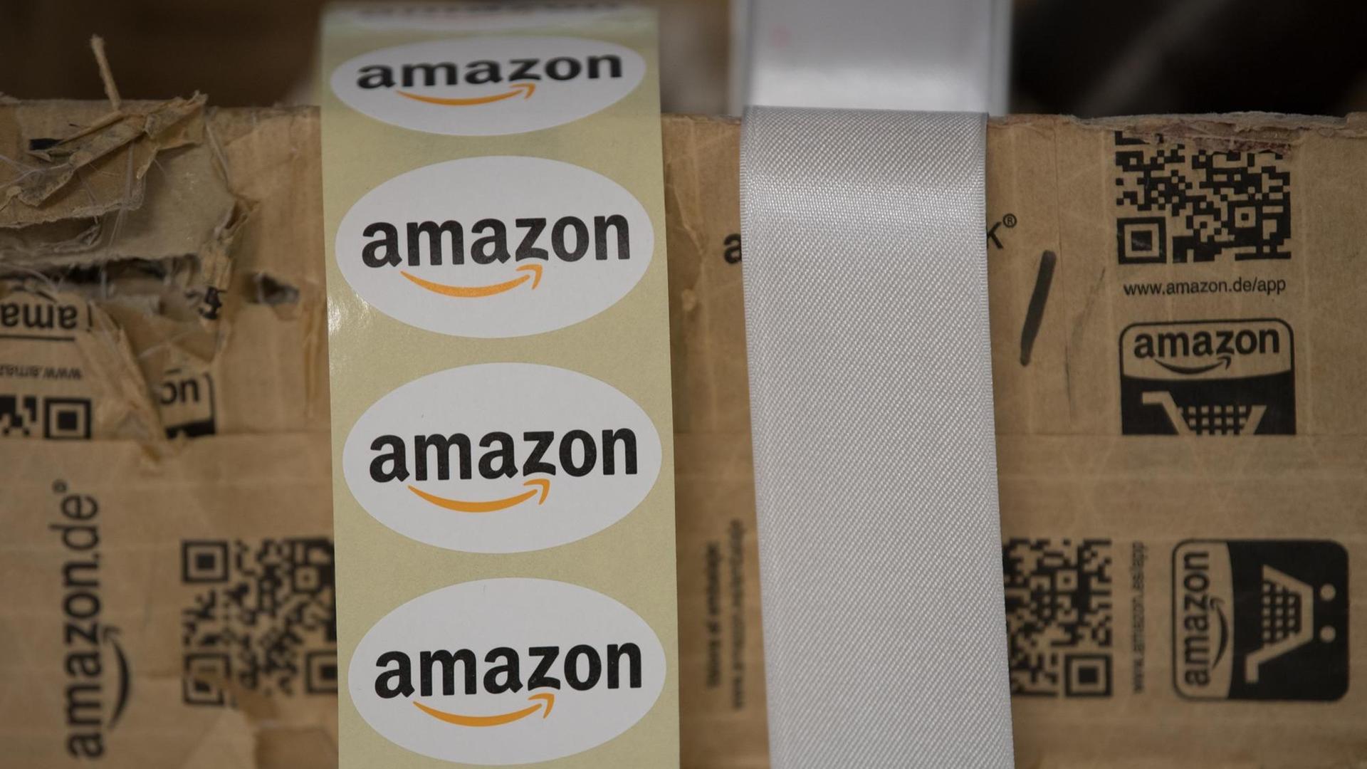 Aufkleber mit der Aufschrift "Amazon" hängen am 07.12.2017 beim Medientag von Versandhändler Amazon in Bad Hersfeld (Hessen) aus einem Versandkarton. Um das umsatzstarke Weihnachtsgeschäft zu bewältigen, hat Versandhändler Amazon bundesweit 13.000 Aushilfen eingestellt.