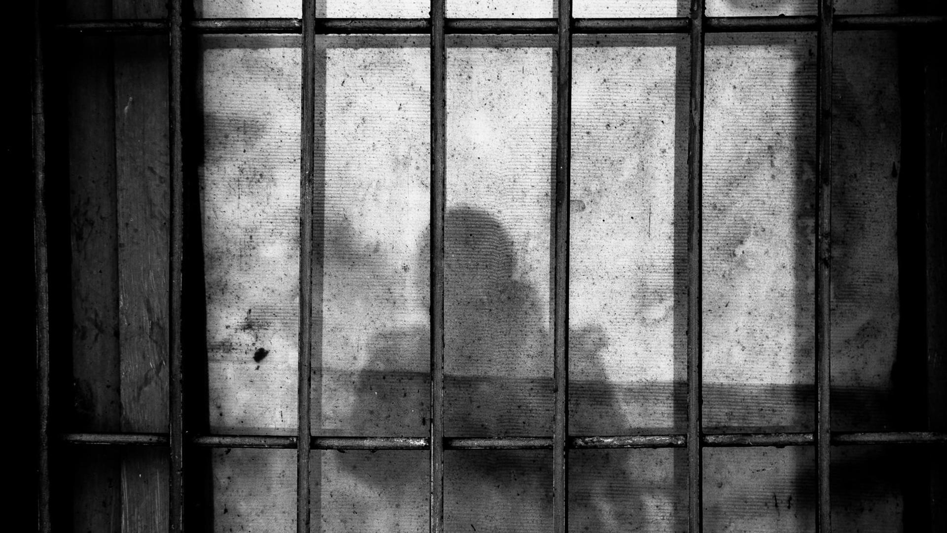 Der Schatten von einem Menschen mit Kind auf dem Arm vor Gefängnisgittern. Der Schatten von einem Menschen mit Kind auf dem Arm vor Gefängnisgittern.