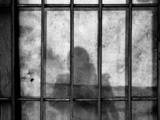 Der Schatten von einem Menschen mit Kind auf dem Arm vor Gefängnisgittern.