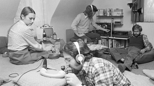 Junge Leute produzieren ein Hörspiel in Göttingen; auf dem schwarz/weiß-Bild sind drei junge Männer und eine Frau zu sehen, die in einem Wohnzimmer O-Ton-Aufnahmen für ein Hörspiel machen.