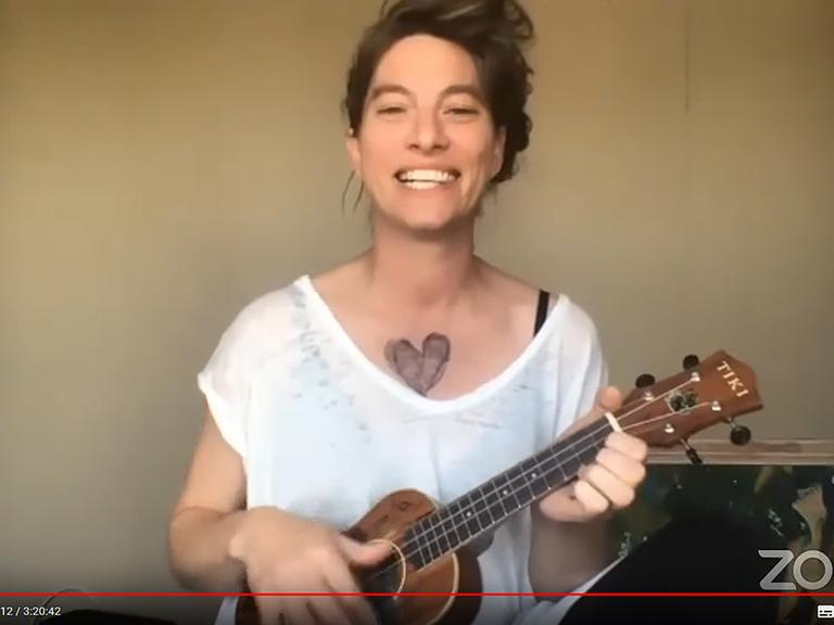 Musikerin Amanda Palmer beteiligte sich mit ihrer Ukulele am Musikmarathon. Eine Frau in einem weißen T-Shirt steht vor einer Kamera und spielt Ukulele.