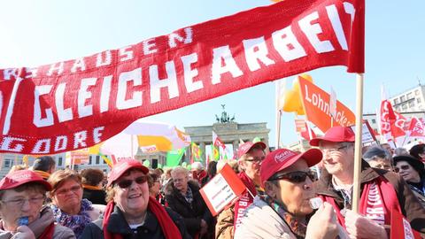 Teilnehmer der Kundgebung des Deutschen Gewerkschaftsbundes DGB stehen am 20.03.2015 am Brandenburger Tor in Berlin anlässlich des "Equal Pay Day" mit Transparenten zusammen.