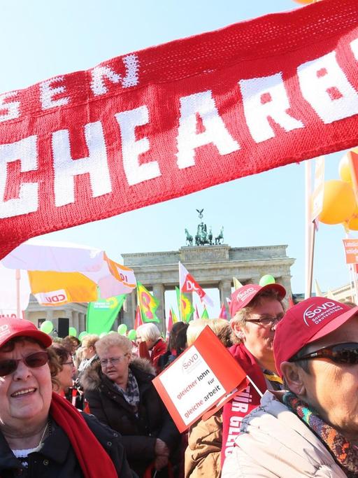 Teilnehmer der Kundgebung des Deutschen Gewerkschaftsbundes DGB stehen am 20.03.2015 am Brandenburger Tor in Berlin anlässlich des "Equal Pay Day" mit Transparenten zusammen.