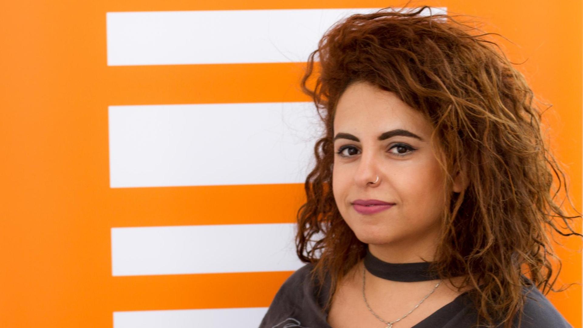 Die syrische Journalistin Hiba Obaid hat lange schwarze Haare und steht vor einer Wand mit dem Deutschlandfunk Kultur Logo. Die syrische Journalistin Hiba Obaid hat lange schwarze Haare und steht vor einer Wand mit dem Deutschlandfunk Kultur Logo.