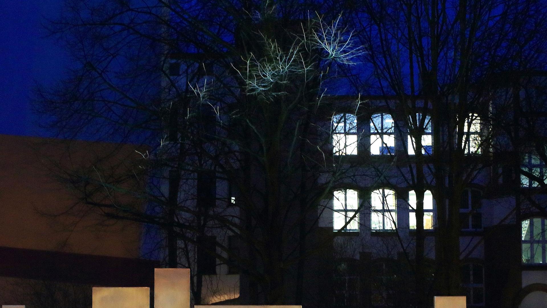 Außenansicht eines Universitätsgebäudes bei Nacht mit hellerleuchteten Fenstern, im Vordergrund der Schriftzug "Universität".