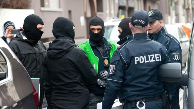 Polizisten stehen bei einer Razzia gegen Islamisten in Berlin neben einem Polizeifahrzeug, in das sie zuvor einen Verdächtigen gebracht hatten.