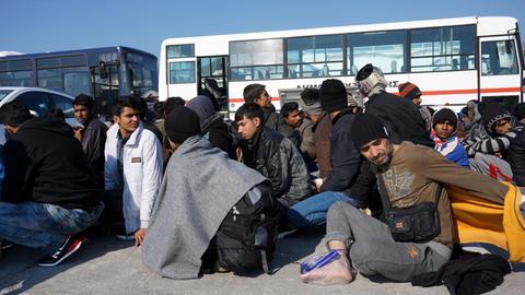 Sie sehen Flüchtlinge auf der griechischen Insel Lesbos. Im Hintergrund sehen Sie Busse.