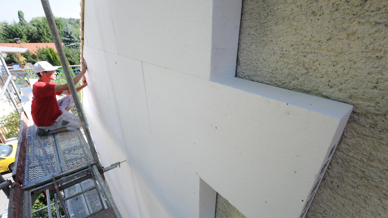 Ein Arbeiter sitzt auf einem Bau-Gerüst und montiert Styropor-Platten an einer Hausfassade. Ein Arbeiter sitzt auf einem Bau-Gerüst und montiert Styropor-Platten an einer Hausfassade.