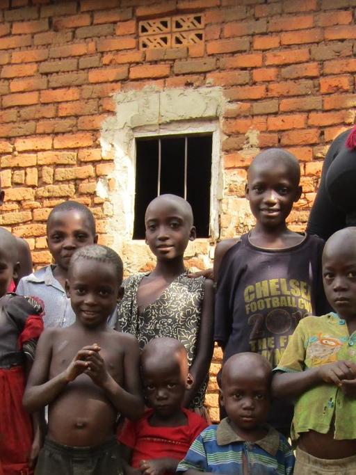 Susan Kigula hilft Kindern von inhaftierten Frauen in Uganda. Sie steht neben einer Gruppe vor einem einfachen Steinhaus.