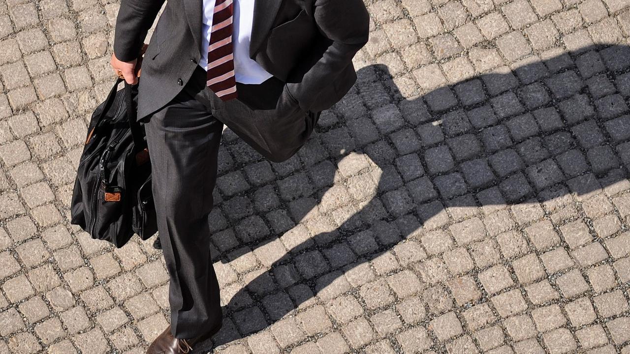 Ein Mann mit Anzug und Aktenkoffer wirft am 17.05.2013 in Berlin einen Schatten auf das Kopfsteinpflaster. Ein Mann mit Anzug und Aktenkoffer wirft am 17.05.2013 in Berlin einen Schatten auf das Kopfsteinpflaster.