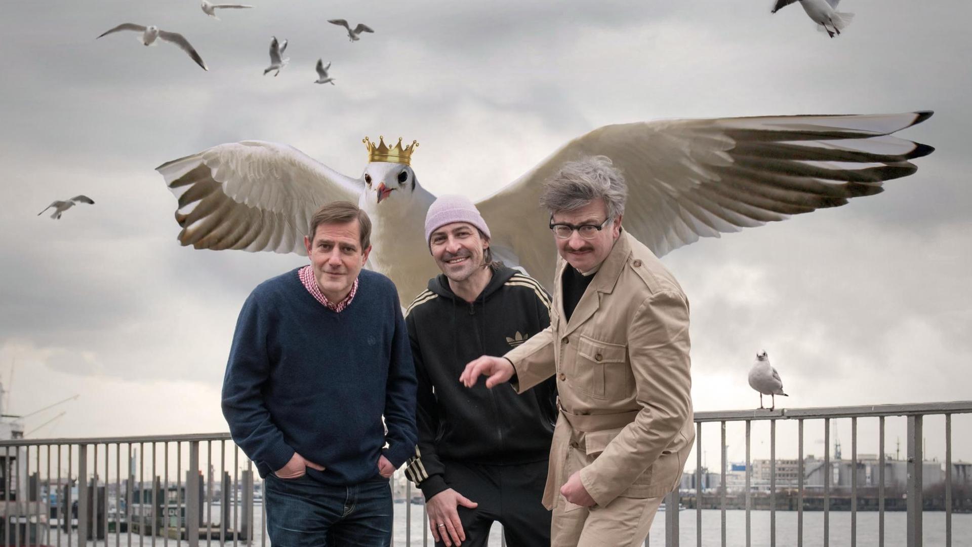 Auf dem Bild sind der Musiker Andreas Dorau, der Autor Gereon Klug und der Regisseur Patrick Wengenroth zu sehen. Hinter ihnen kommt eine computergenerierte Möwe angeflogen. Auf dem Kopf trägt sie eine Krone Auf dem Bild sind der Musiker Andreas Dorau, der Autor Gereon Klug und der Regisseur Patrick Wengenroth zu sehen. Hinter ihnen kommt eine computergenerierte Möwe angeflogen. Auf dem Kopf trägt sie eine Krone