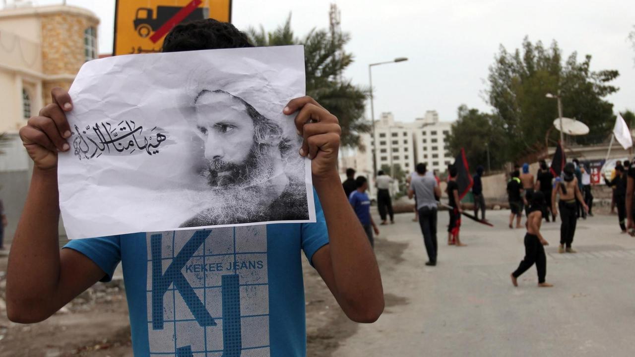 Ein Mann hält sich ein Foto von Nimr al-Nimr vors Gesicht.