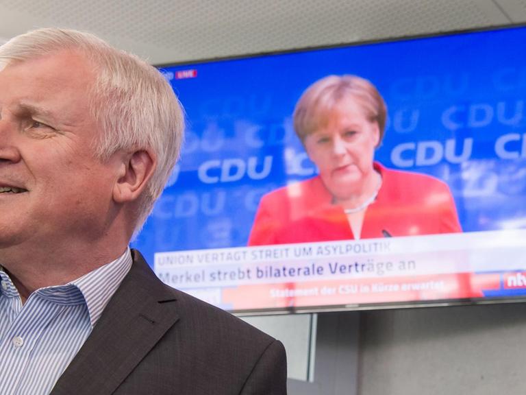 Horst Seehofer, CSU-Vorsitzender und Bundesminister für Inneres, Heimat und Bau, läuft auf seinem Weg zu einer Pressekonferenz, die in Anschluss an die Sitzung des CSU-Vorstands stattfindet, an einem Fernseher vorbei, auf dem die Pressekonferenz von Bundeskanzlerin Angela Merkel (CDU) übertragen wird.