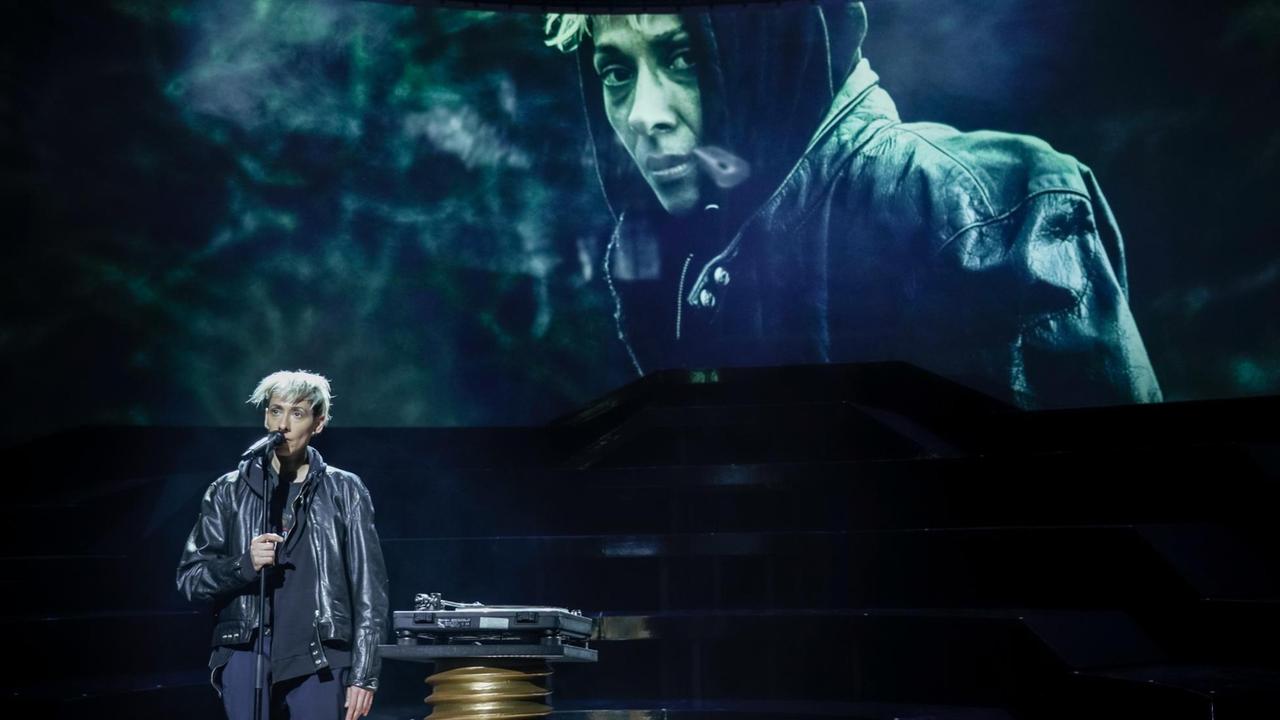 Der Roman "Das Leben des Vernon Subutex" als Theaterstück in den Münchner Kammerspielen. Das Szenenfoto zeigt die Darstellerin Jelena Kuljić. Sie steht vor einer Leinwand auf der sie selbst vergrößert zu sehen ist. Der Roman "Das Leben des Vernon Subutex" als Theaterstück in den Münchner Kammerspielen. Das Szenenfoto zeigt die Darstellerin Jelena Kuljić. Sie steht vor einer Leinwand auf der sie selbst vergrößert zu sehen ist.