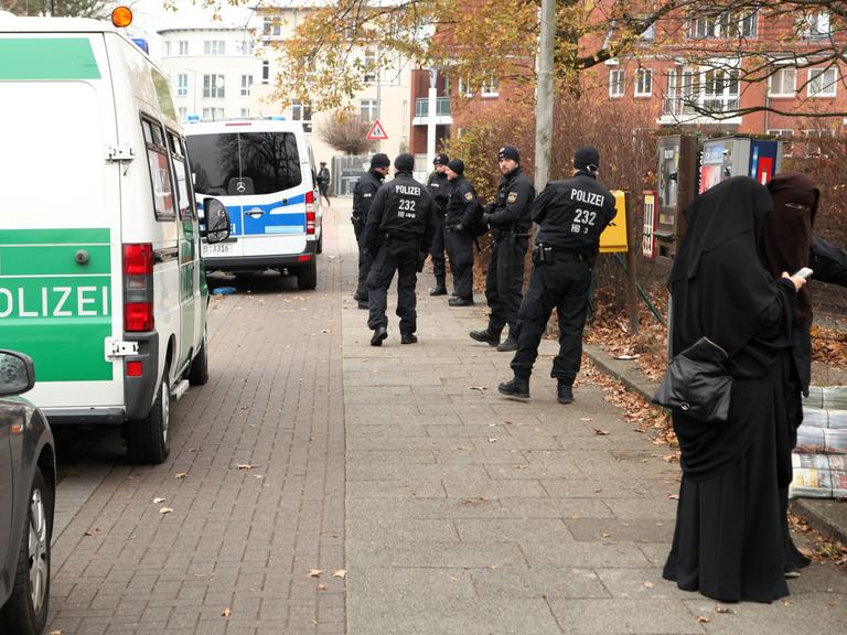 Polizeiwagen und Beamte stehen in Bremen während einer Durchsuchung vor dem salafistischen Kultur & Familien Verein (KuF) im Stadtteil Gröpelingen neben zwei Frauen, die vollkommen verschleiert sind.