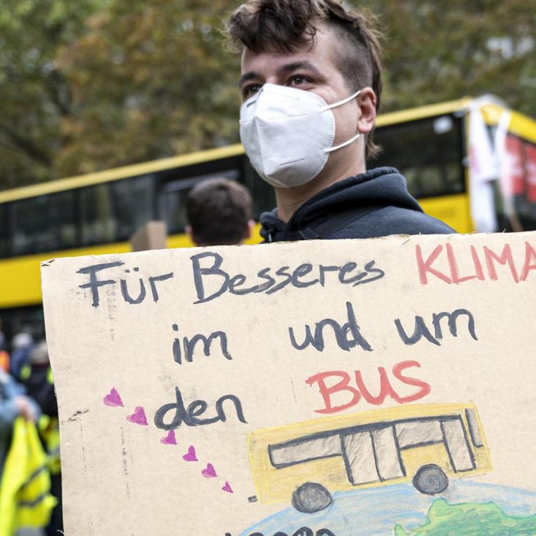 Ein Aktivist von Friday for Future steht vor dem BVG Betriebshof Cicerostraße mit einem Plakat mit der Aufschrift "Für besseres Klima im und um den Bus". Mit der Aktion will die Gewerkschaft Verdi den Druck auf die Arbeitgeber bei den anstehenden Tarifverhandlungen erhöhen.