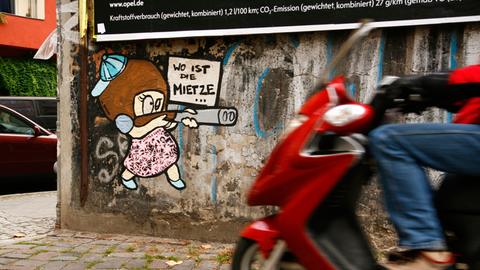 Ein Vespa-Fahrer vor einem Motiv des Street-Art-Künstlers "El Bocho" - "Little Lucy", die mit der Schrotflinte in der Hand ihre Katze jagt, aufgenommen in Berlin im Bezirk Prenzlauer Berg im Oktober 2011.
