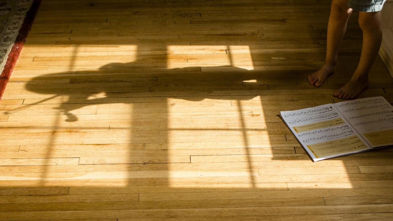 Der Schatten eines Mädchens, das Geige spielt, der sich auf einem Holzfußboden zeigt.