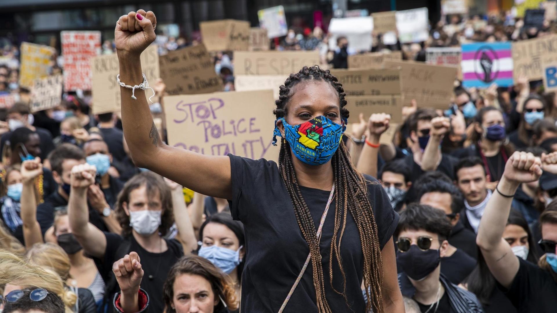 Eine schwarze Frau und viele Demonstranten heben die Faust als Zeichen gegen Rassismus. Eine schwarze Frau und viele Demonstranten heben die Faust als Zeichen gegen Rassismus.