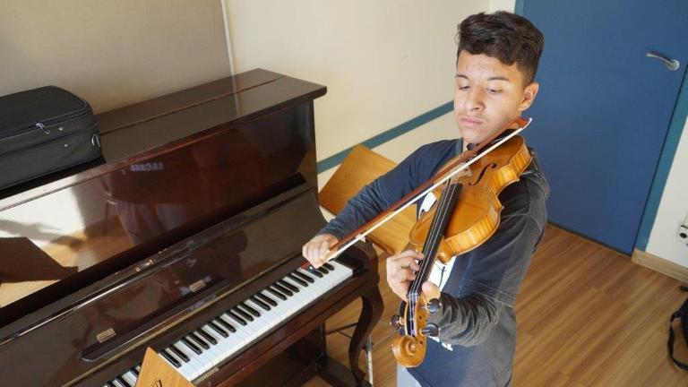 Ein junger Mann spielt neben einem Klavier auf einer Geige Ein junger Mann spielt neben einem Klavier auf einer Geige