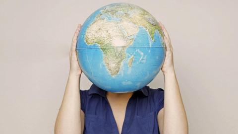 Eine Frau versteckt ihren Kopf hinter einem Globus.