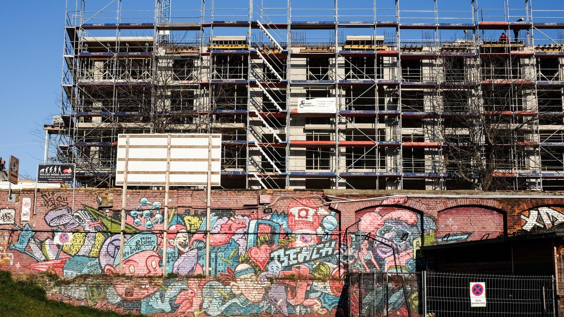Eine Mauer mit bunten Graffiti vor einer Baustelle.