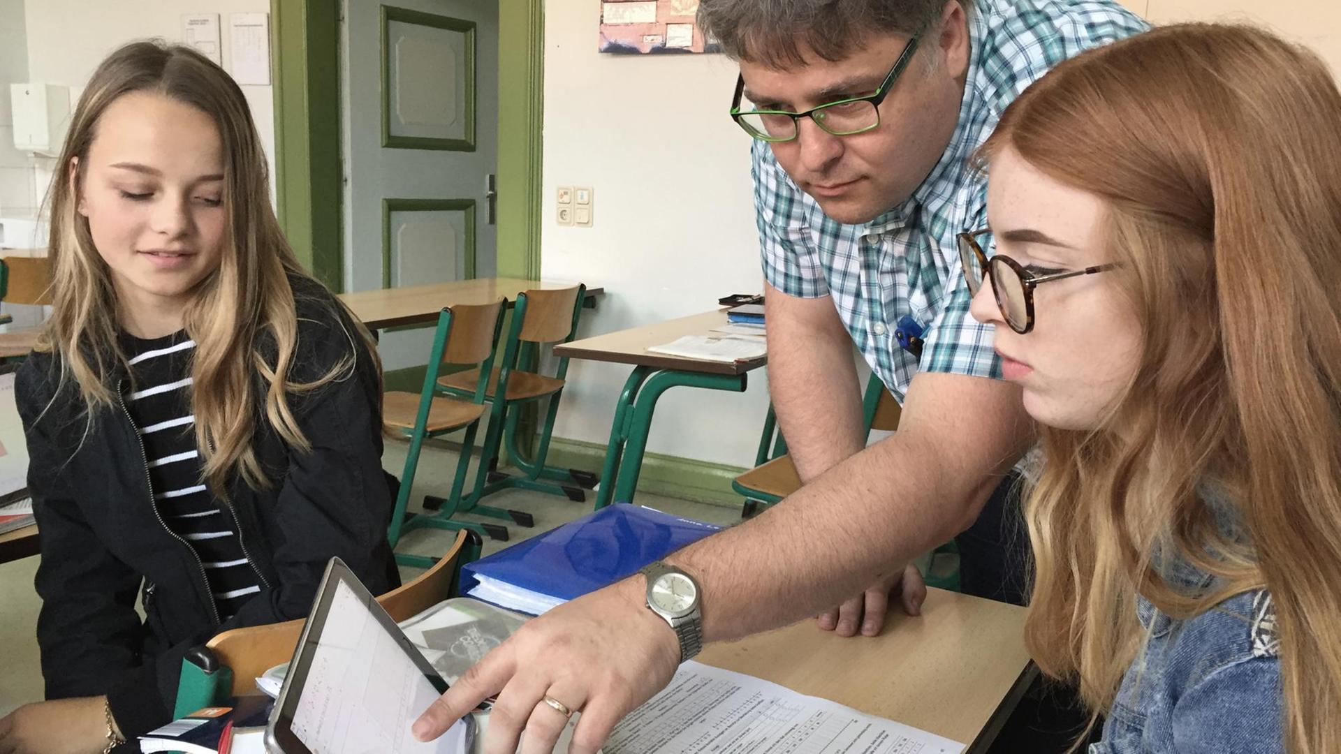 Mathelehrer Horst Kretschmer zeigt zwei Schülerinnen etwas auf dem Tablet. Mathelehrer Horst Kretschmer zeigt zwei Schülerinnen etwas auf dem Tablet.