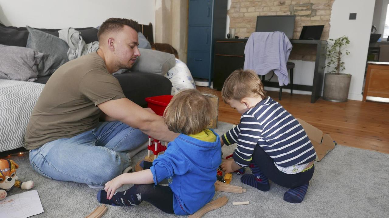 Ein junger Vater sitzt am Boden und spielt mit seinen zwei kleinen Kindern. Ein junger Vater sitzt am Boden und spielt mit seinen zwei kleinen Kindern.