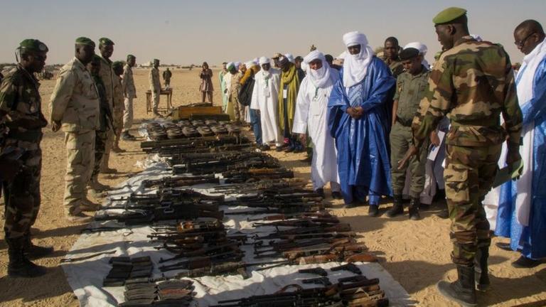 Teilnehmer des Friedensforums begutachten die Waffen, die auf dem Boden liegen Teilnehmer des Friedensforums begutachten die Waffen, die auf dem Boden liegen