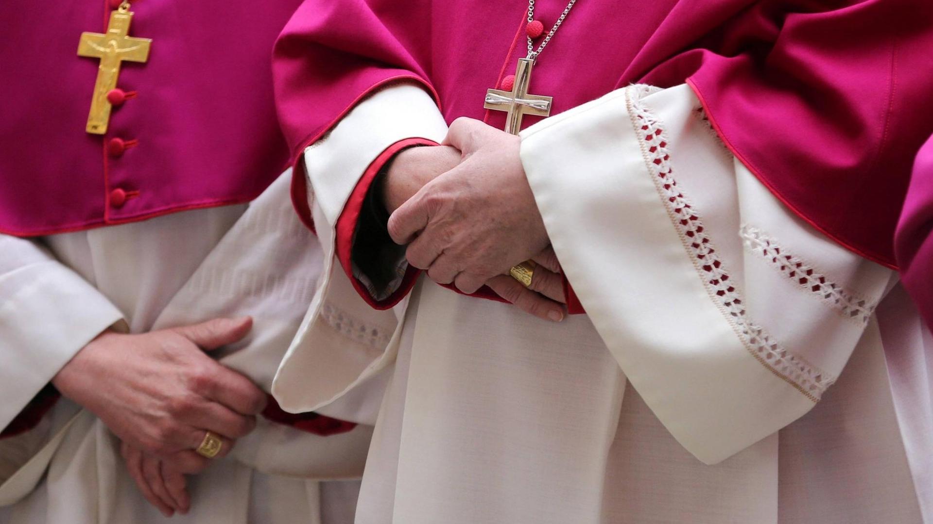Im Anschnitt fotografierte Würdenträger der katholischen Kirche, sie halten ihre Hände gekreuzt und tragen purpurrote Roben und große Kreuzanhänger um den Hals Im Anschnitt fotografierte Würdenträger der katholischen Kirche, sie halten ihre Hände gekreuzt und tragen purpurrote Roben und große Kreuzanhänger um den Hals