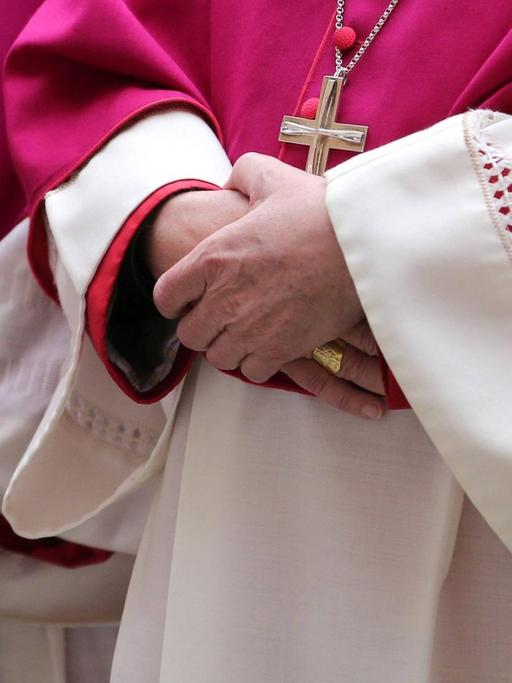 Im Anschnitt fotografierte Würdenträger der katholischen Kirche, sie halten ihre Hände gekreuzt und tragen purpurrote Roben und große Kreuzanhänger um den Hals