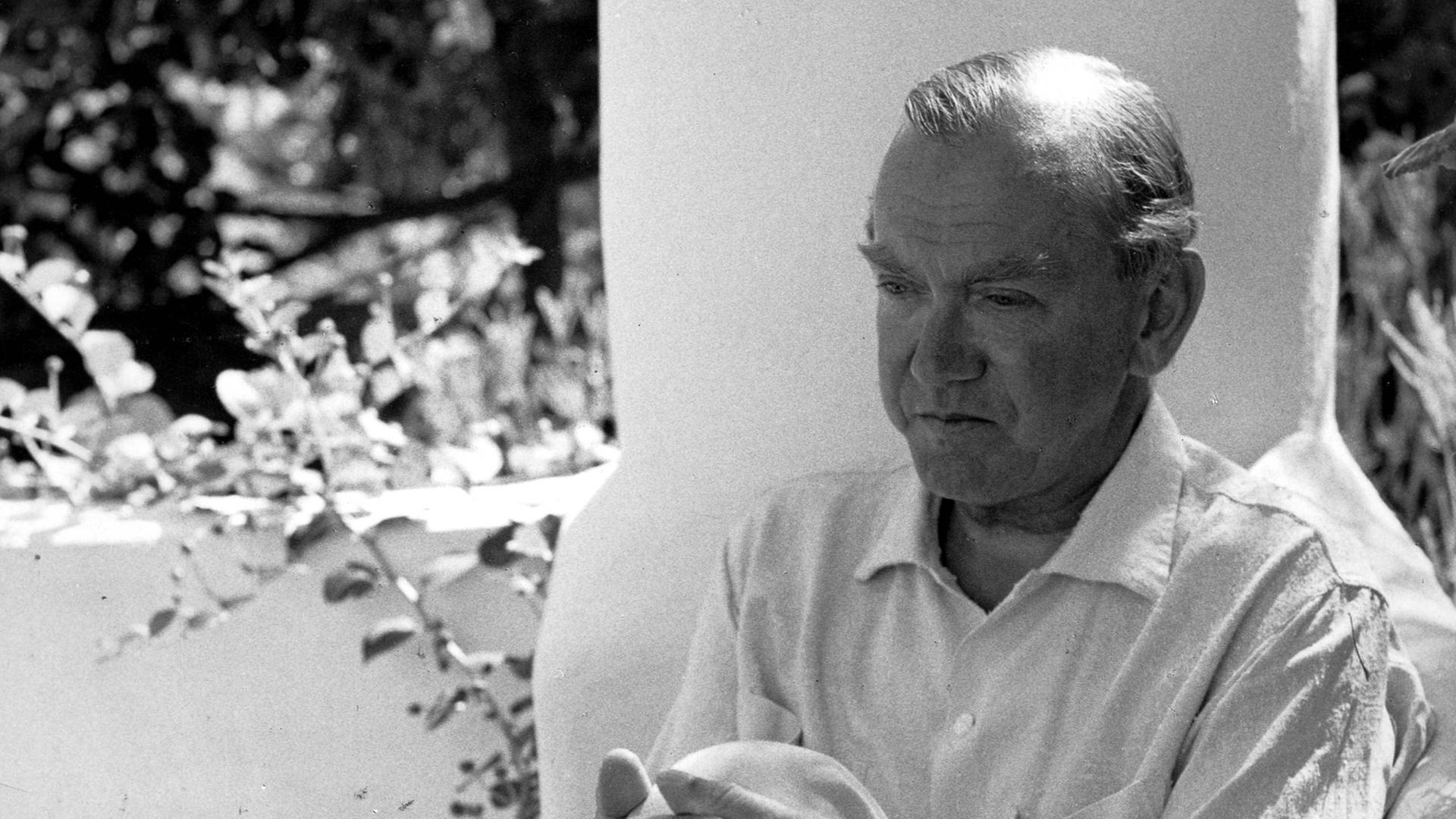 Graham Greene sitzt auf einer Terrasse im Garten. Graham Greene sitzt auf einer Terrasse im Garten.