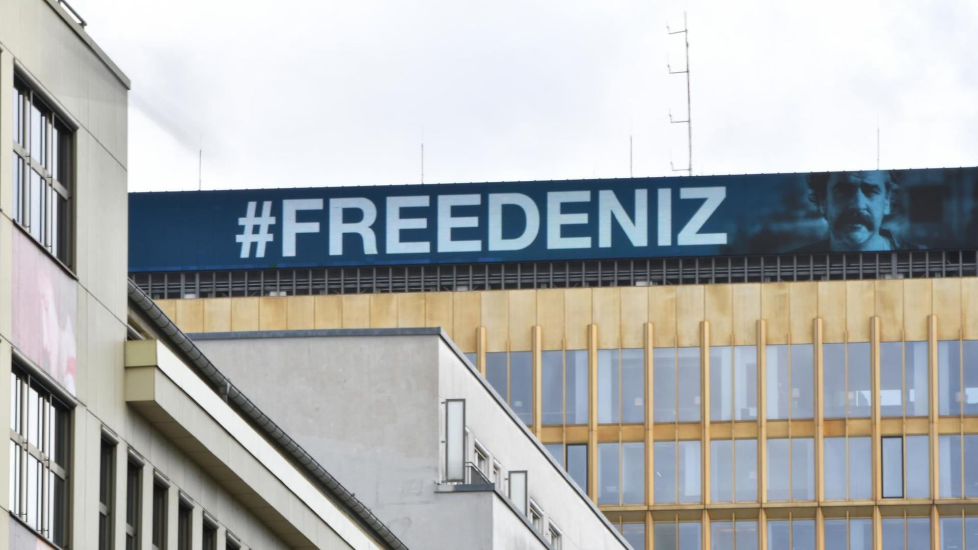 #FREEDENIZ steht in weißer Schrift auf blauem Untergrund am Dach der Konzernzentrale der Springer SE. Daneben das Konterfei von Deniz Yücel.
