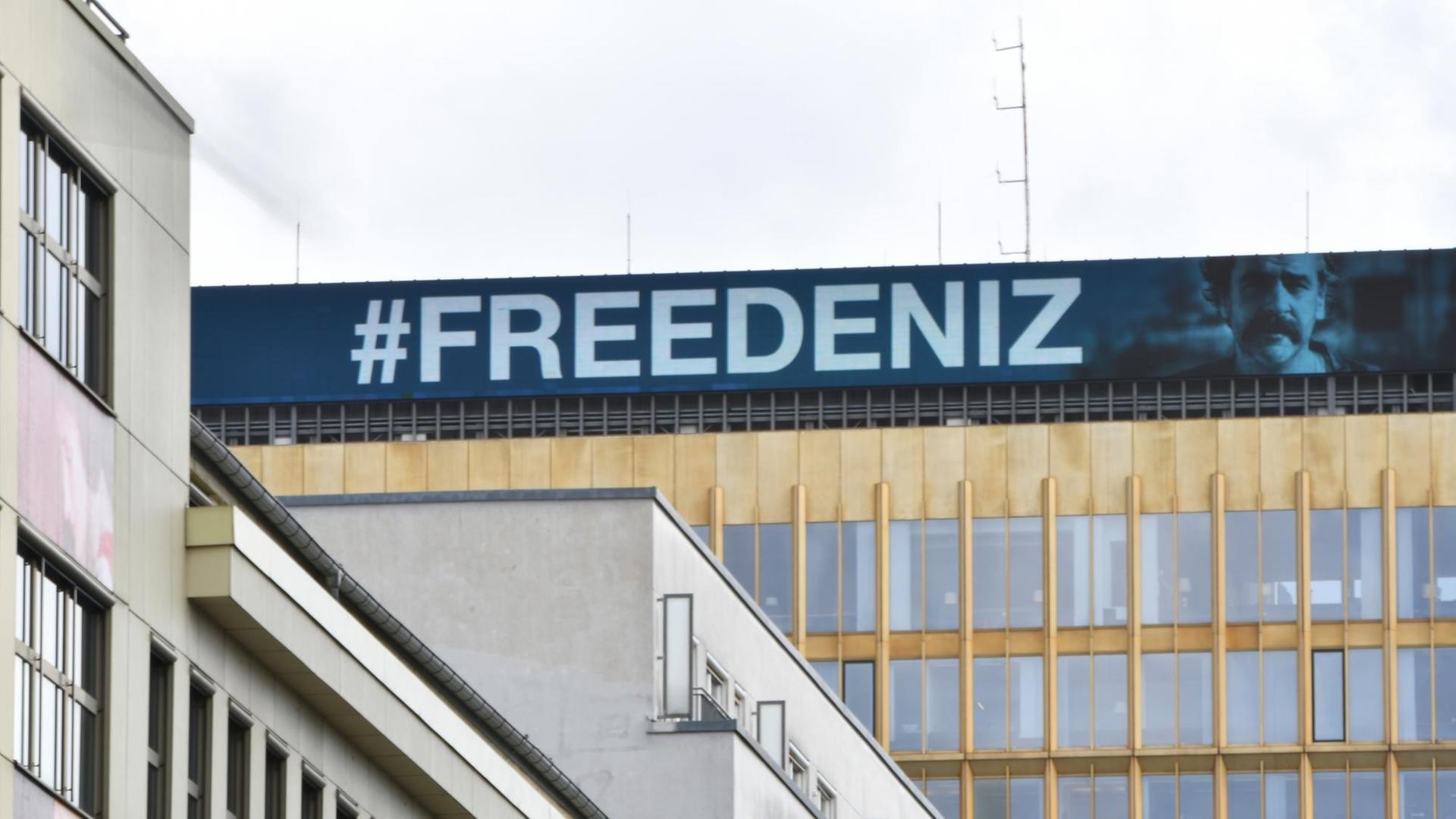 #FREEDENIZ steht in weißer Schrift auf blauem Untergrund am Dach der Konzernzentrale der Springer SE. Daneben das Konterfei von Deniz Yücel. #FREEDENIZ steht in weißer Schrift auf blauem Untergrund am Dach der Konzernzentrale der Springer SE. Daneben das Konterfei von Deniz Yücel.
