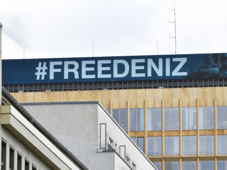 #FREEDENIZ steht in weißer Schrift auf blauem Untergrund am Dach der Konzernzentrale der Springer SE. Daneben das Konterfei von Deniz Yücel.