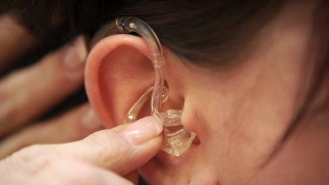Ein Ohr mit einem Ohrring, in das ein Hörgerät eingesetzt wird.