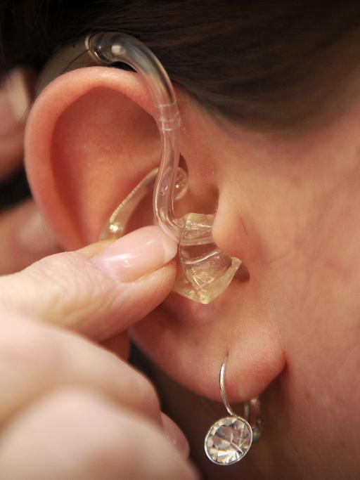 Ein Ohr mit einem Ohrring, in das ein Hörgerät eingesetzt wird.
