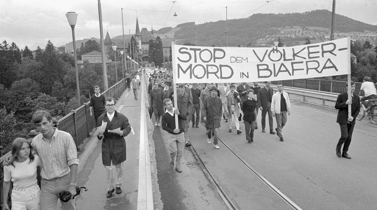 Mit einem Transparent, auf dem "Stop dem Völkermord in Biafra" steht, ziehen einige Demonstranten über eine Brücke. Mit einem Transparent, auf dem "Stop dem Völkermord in Biafra" steht, ziehen einige Demonstranten über eine Brücke.