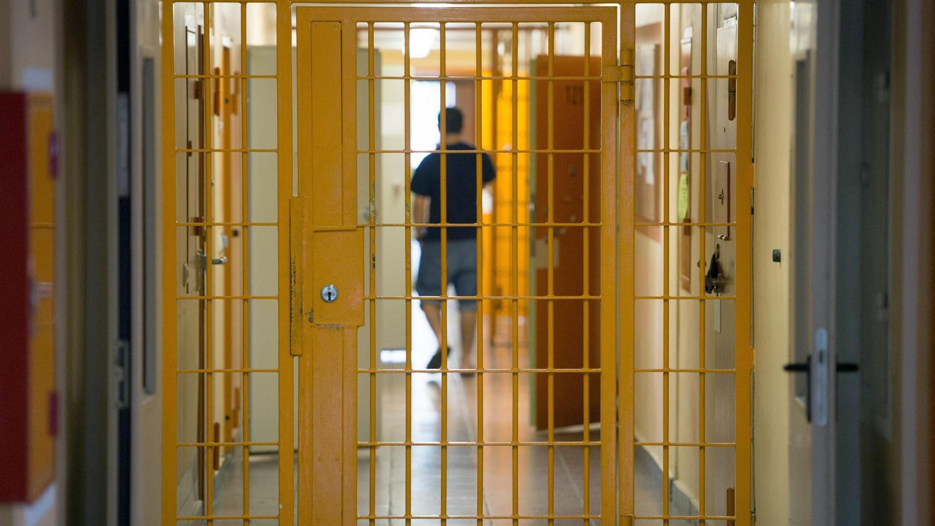 Ein Mann geht am 04.09.2015 in der Justizvollzugsanstalt Hohenleuben in Thüringen hinter einer verschlossenen Gittertür einen Gang entlang.