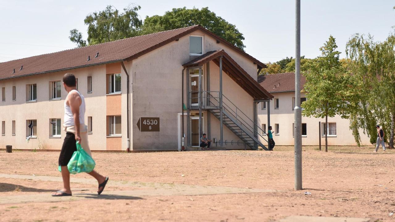 Ein Flüchtling geht am 06.08.2015 in Heidelberg (Baden-Württemberg) in der Flüchtlingsunterkunft Patrick-Henry-Village an Wohnhäusern vorbei.