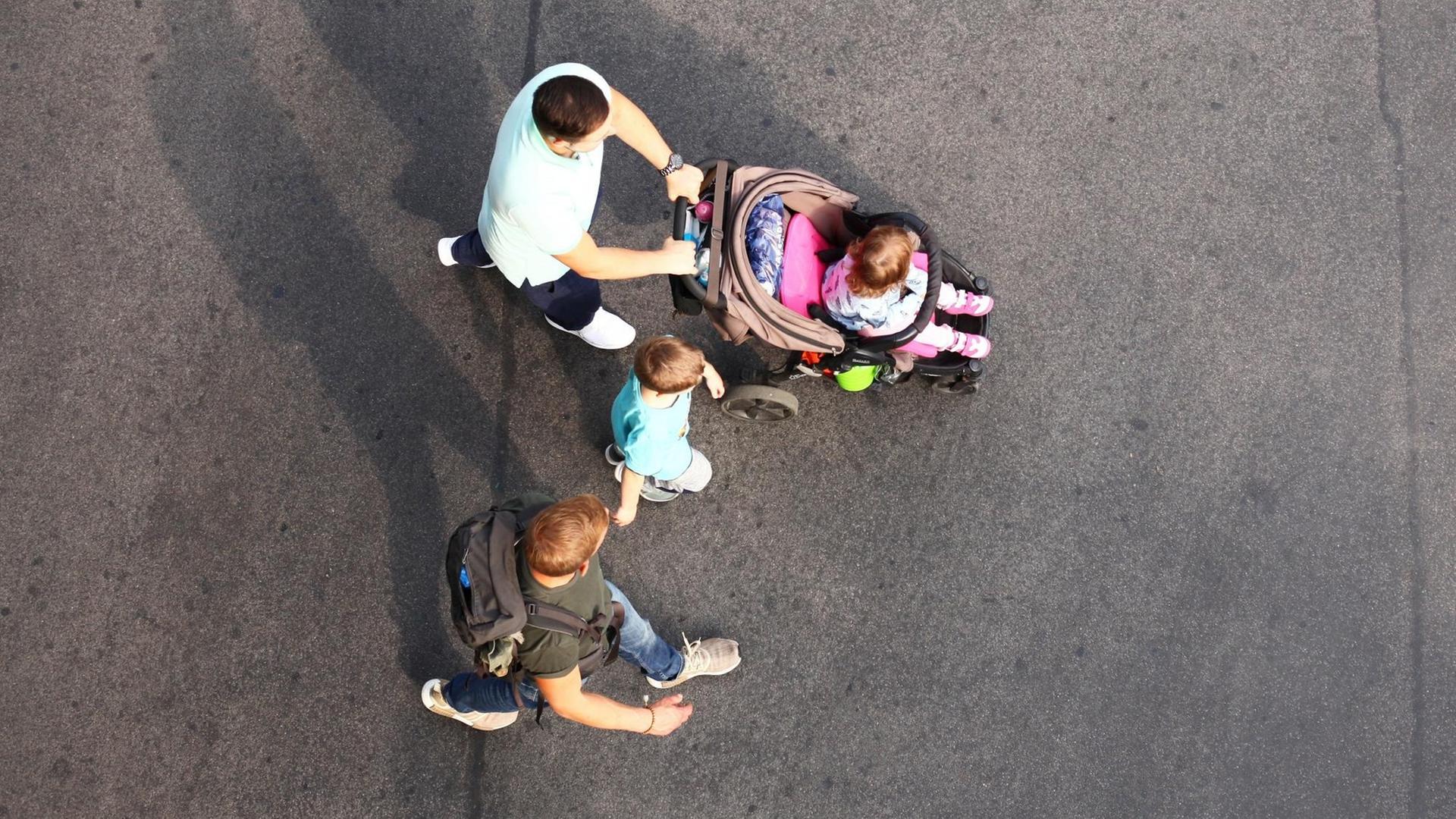 Zwei junge Männer gehen mit zwei Kindern über eine Straße. Zwei junge Männer gehen mit zwei Kindern über eine Straße.