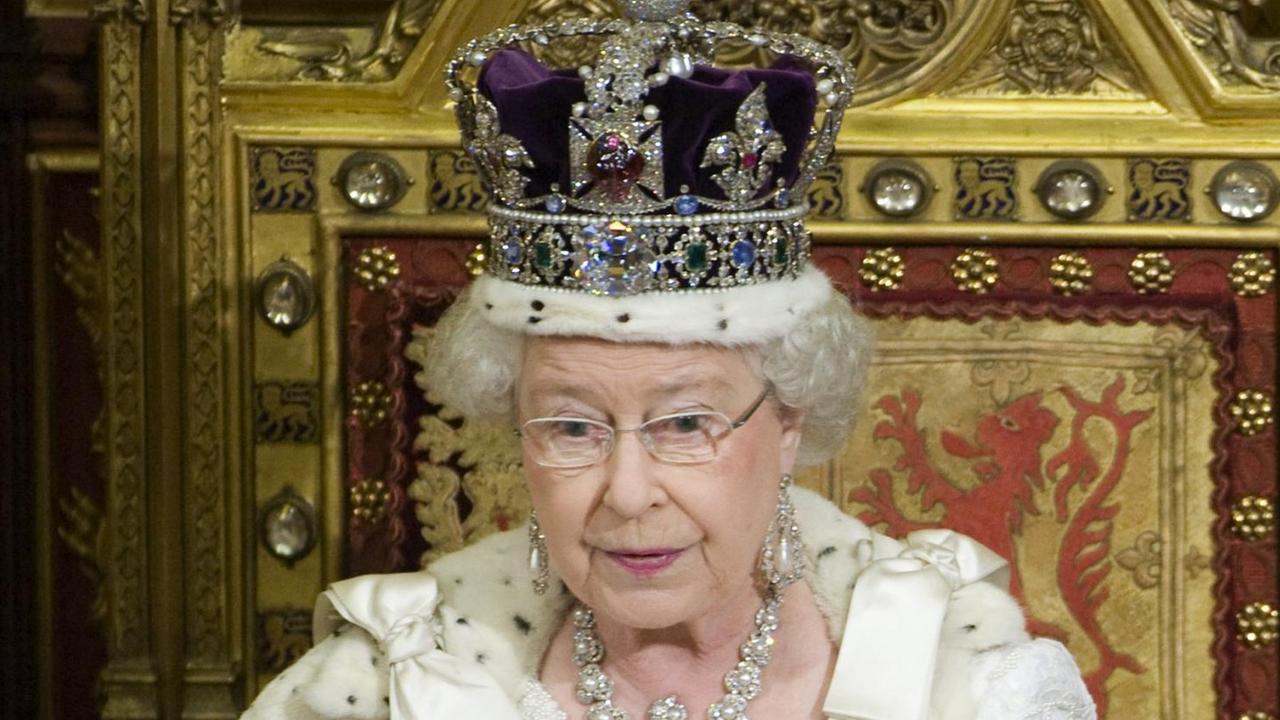 Die Queen sitzt mit Krone und Umhang auf ihrem Thron im Oberhaus und hält das weiße Regierungsprogramm in den Händen, aus dem sie vorliest Die Queen sitzt mit Krone und Umhang auf ihrem Thron im Oberhaus und hält das weiße Regierungsprogramm in den Händen, aus dem sie vorliest