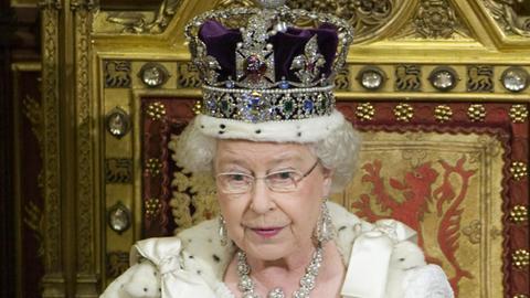 Die Queen sitzt mit Krone und Umhang auf ihrem Thron im Oberhaus und hält das weiße Regierungsprogramm in den Händen, aus dem sie vorliest