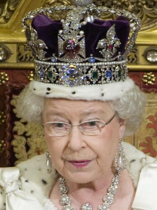 Die Queen sitzt mit Krone und Umhang auf ihrem Thron im Oberhaus und hält das weiße Regierungsprogramm in den Händen, aus dem sie vorliest