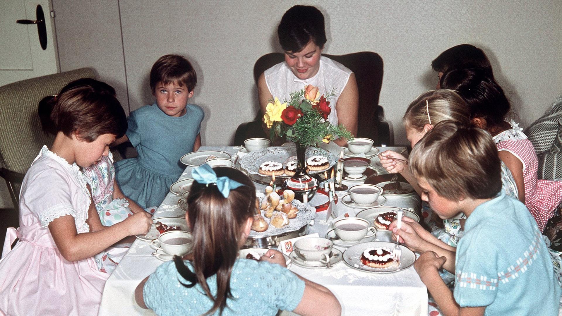 Die kleinen Gäste eines Kindergeburtstages sitzen am Kaffeetisch und essen kleine Törtchen zum Kakao. Die kleinen Gäste eines Kindergeburtstages sitzen am Kaffeetisch und essen kleine Törtchen zum Kakao.