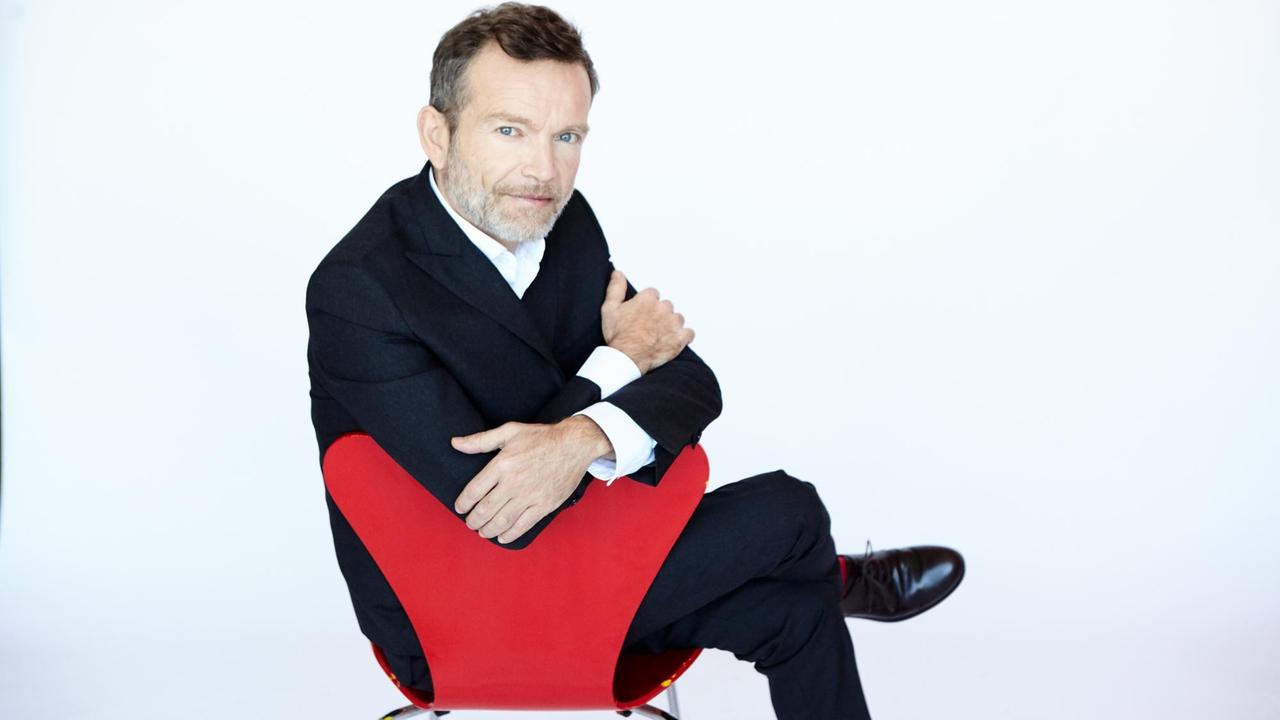 Der Cembalist und Dirigent Christophe Rousset auf einem roten Designer-Stuhl Der Cembalist und Dirigent Christophe Rousset auf einem roten Designer-Stuhl