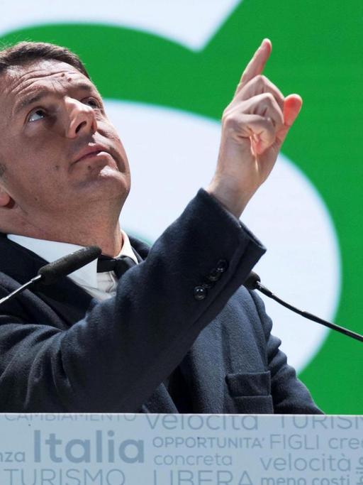 Renzi steht an einem Mikrofon vor einem grünen Plakat mit einer riesigen "Si"-Aufschrift und deutet mit dem Finger nach oben.