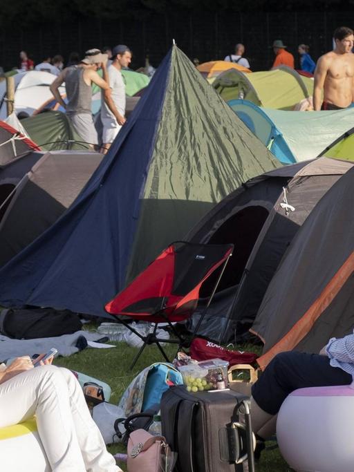 Zwei weibliche Tennis-Fans sitzen bequem in ihren mitgebrachten aufblasbaren Sitzmöbeln. Im Hintergrund: Zelte auf dem Camping-Platz von Wimbledon.