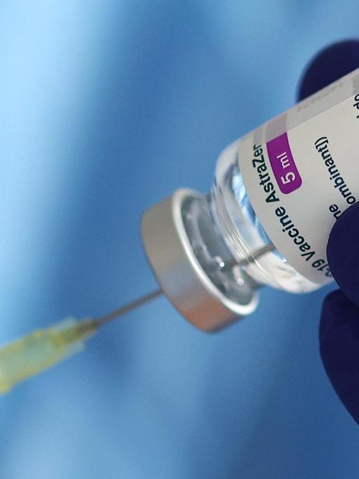Ein blau behandschuhte Hand hält ein Fläschchen mit dem Covid-Impfstoff von AstraZeneca und präpariert eine Spritze.